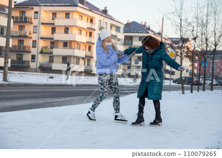 The girl wobbles while standing in the snow and a friend has to support her. 110079265