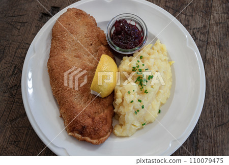 Pork escalope Viennese style from straw pork - in crispy breading served with homemade potato salad, lemon and cranberries. 110079475