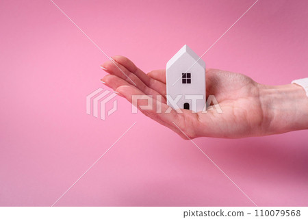 Female hands, a small wooden house and keys as an idea for investing in your own home and achieving the goal of buying real estate 110079568