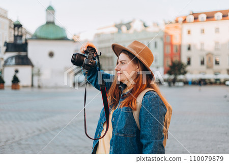 Happy young European tourist with backpack in hat makes photo or video on camera on Market Square in Krakow. Traveling Europe in summer. Vacation concept 110079879