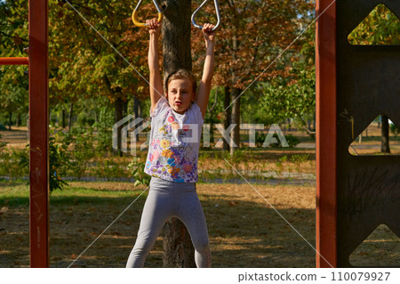A cheerful child girl is working out on the horizontal bar, sports apparatus 110079927