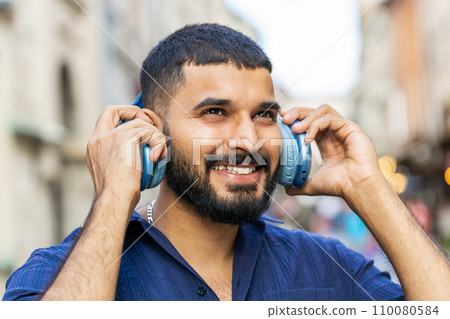 Happy young man in wireless headphones choosing, listening music dancing outdoors city street 110080584
