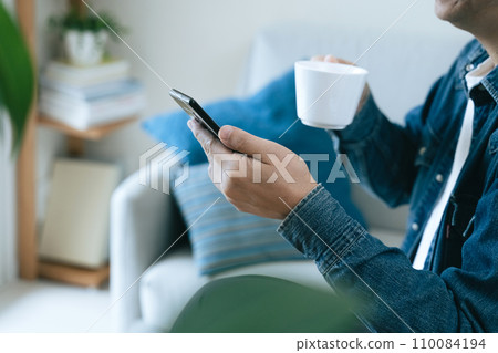 一名男子一邊喝著牛奶咖啡，一邊看著智慧型手機 110084194