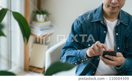 Middle-aged man operating a smartphone at home Middle-aged man operating a smartphone at home 110084309