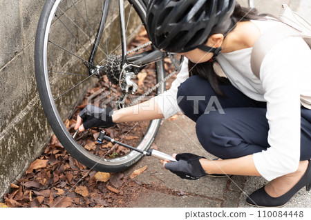 Young woman putting on and taking off a valve cap on a road bike to repair a puncture 110084448