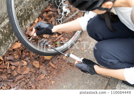 Young woman putting on and taking off a valve cap on a road bike to repair a puncture 110084449