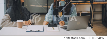 Woman recording a podcast on her laptop computer with headphones and a microscope. Female podcaster making audio podcast from her home studio. 110085897