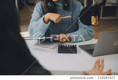 Woman recording a podcast on her laptop computer with headphones and a microscope. Female podcaster making audio podcast from her home studio. Woman recording a podcast on her laptop computer with headphones and a microscope. Female podcaster making audio podcast from her home studio. 110085927