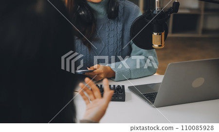 Woman recording a podcast on her laptop computer with headphones and a microscope. Female podcaster making audio podcast from her home studio. 110085928