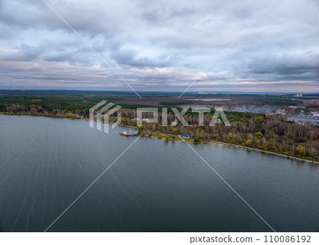 Colorful autumn forest with trees on the shore of a blue lake - top aerial view. 110086192