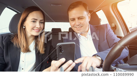 Office worker sits in car and shows to colleague phone screen Office worker sits in car and shows to colleague phone screen 110089990