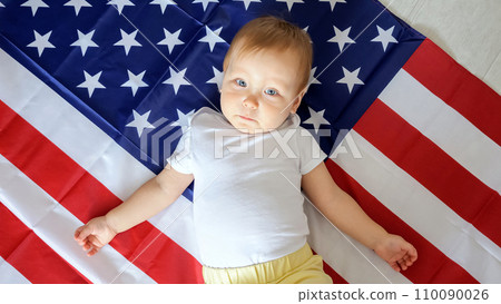 Cheerful toddler lies on blanket as flag of USA in light studio 110090026