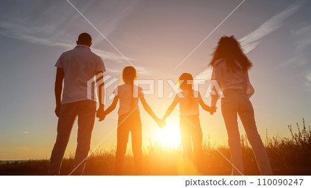 Sun rays fall on family holding hands in field at sunset 110090247