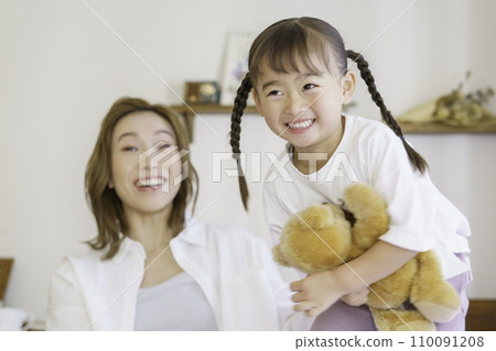 A 4-year-old girl jumps with a teddy bear and a brown-haired young mother laughs at her. A 4-year-old girl jumps with a teddy bear and a brown-haired young mother laughs at her. 110091208