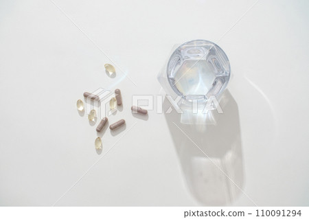 A glass of water on a white background with capsules. Capsule medicine is a form of divided dosage medicine with ingredients including capsule shell (made of starch, gelatin, HPMC, ...). A glass of water on a white background with capsules. Capsule medicine is a form of divided dosage medicine with ingredients including capsule shell (made of starch, gelatin, HPMC, ...). 110091294