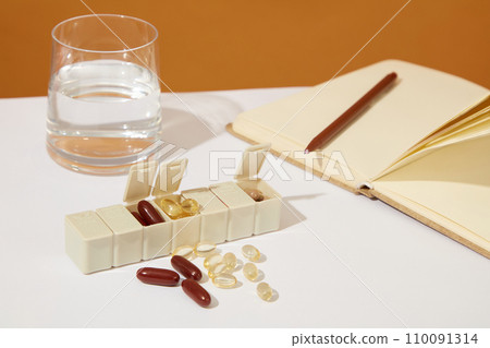A glass of water, a daily pill box and dietary supplements on a white background. Adding dietary supplements to daily diet helps your body provide enough nutrients. 110091314