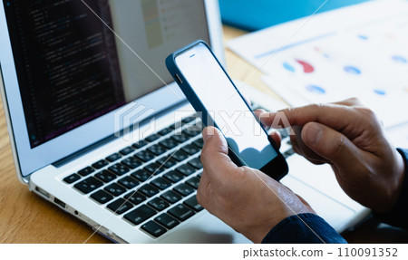 Hands of a man operating a computer and smartphone 110091352