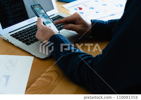 Hands of a man operating a computer and smartphone 110091358