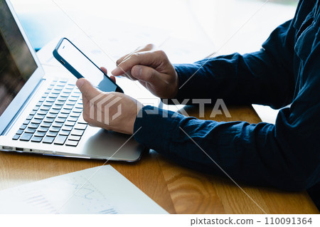 Hands of a man operating a computer and smartphone 110091364