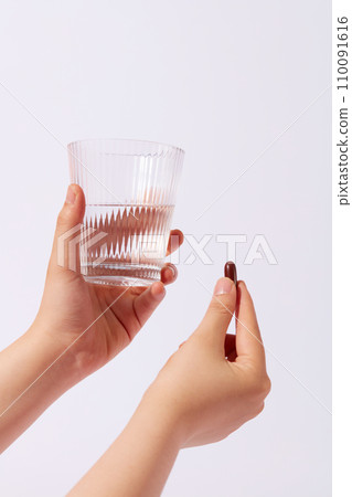 Front view of a glass of water in one hand and a capsule in the other on a white background. Using dietary supplements helps the body get enough nutrients. Medicine concept. Front view of a glass of water in one hand and a capsule in the other on a white background. Using dietary supplements helps the body get enough nutrients. Medicine concept. 110091616