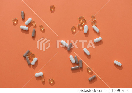 Vitamin E capsules, gray capsules and white tablets are randomly decorated on an orange background. Images used for advertising with medicine theme. 110091634