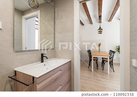 View from the bathroom with a sink and a mirror to the kitchen living area with a table and chairs waiting for the tenants. Concept of real estate and the work of realtors with new apartments View from the bathroom with a sink and a mirror to the kitchen living area with a table and chairs waiting for the tenants. Concept of real estate and the work of realtors with new apartments 110092338