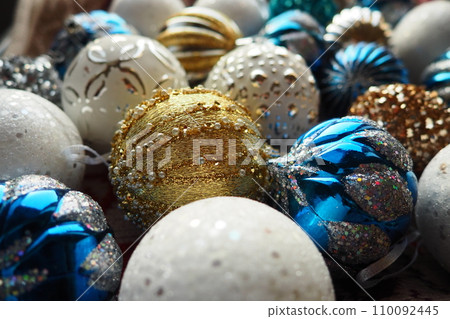 New Year's Christmas balls and decorations close up. A lot of decoration of golden, blue, yellow, white, silver. Striped Christmas balls lie on surface. Festive beautiful colorful background. Design. 110092445