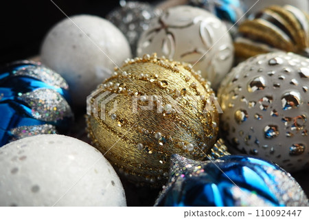New Year's Christmas balls and decorations close up. A lot of decoration of golden, blue, yellow, white, silver. Striped Christmas balls lie on surface. Festive beautiful colorful background. Design. 110092447