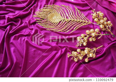 Purple pink lilac violet silk fabric texture background. Beautiful folds on the twisted material. Golden New Year Christmas decorations, Firebird feather, berries and twigs. Copy space. Xmas design 110092479