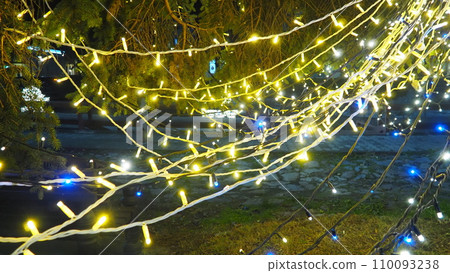 New Year glowing golden garlands hang over Christmas tree. Outdoor winter decoration. Festive design of city square. Garlands blink and sway. Bokeh flickering light bulbs. Festival Noel xmas good mood 110093238