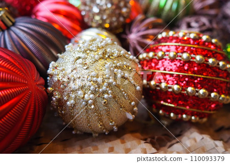 New Year's Christmas balls and decorations close up. A lot of decor of gold, red, yellow, brown, green, silver. Striped Christmas balls lie in a bunch. Festive beautiful colorful background. Design 110093379