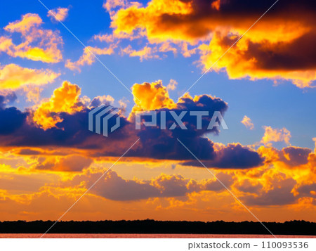Beautiful sunset sky above clouds with dramatic light. Yellow, orange, red clouds above the horizon. Beautiful evening sky landscape. Sunset over the sea. Generated by artificial intelligence. 110093536
