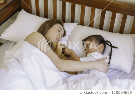 Young brown-haired mom tucking her baby girl into bed 110094699