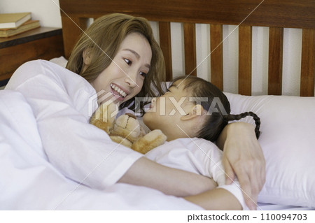 Young brown-haired mom tucking her baby girl into bed 110094703