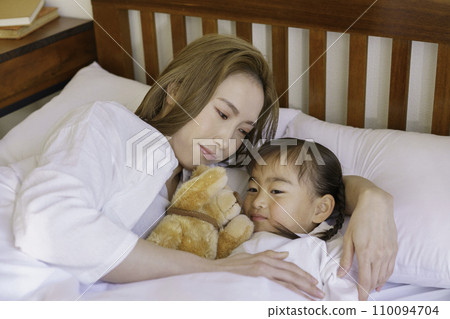 Young brown-haired mom tucking her baby girl into bed 110094704
