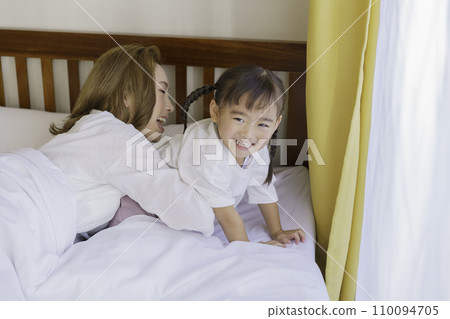 A young brown-haired mother tries to lull her 4-year-old girl to sleep when she tries to get up in bed. 110094705
