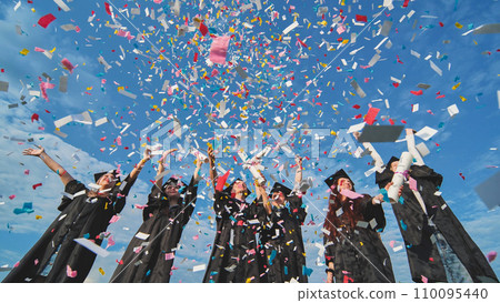 Happy graduates throw colorful confetti against a blue sky. Happy graduates throw colorful confetti against a blue sky. 110095440