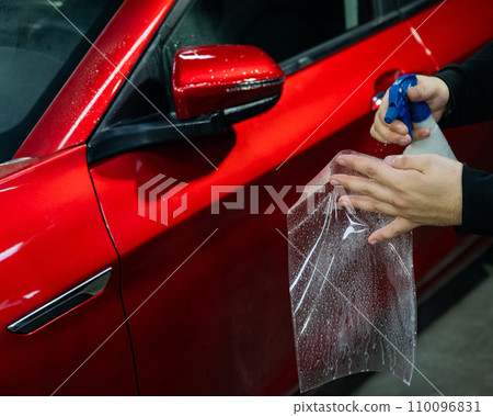 A technician sprays water before applying protective vinyl film to a car. A technician sprays water before applying protective vinyl film to a car. 110096831