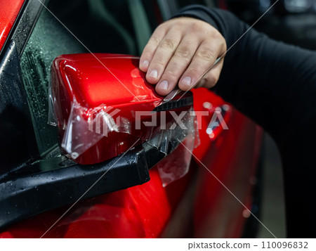 The master applies vinyl film to the side view mirror of a car.  110096832