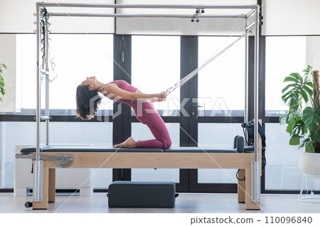 Asian woman doing Pilates on reformer machine.  110096840