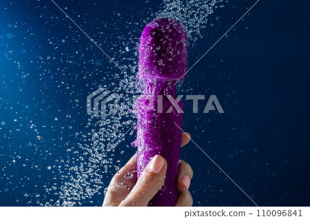 A woman washes a purple vibrator under the shower. Waterproof sex toy on a blue background. A woman washes a purple vibrator under the shower. Waterproof sex toy on a blue background. 110096841