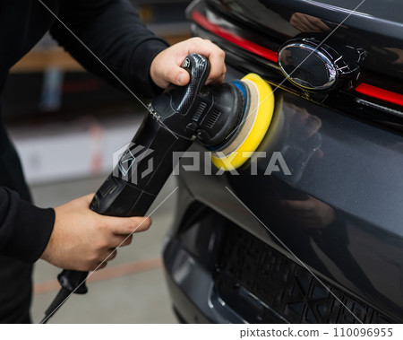 A mechanic polishes the surface of a car trunk door with a grinding machine. A mechanic polishes the surface of a car trunk door with a grinding machine. 110096955