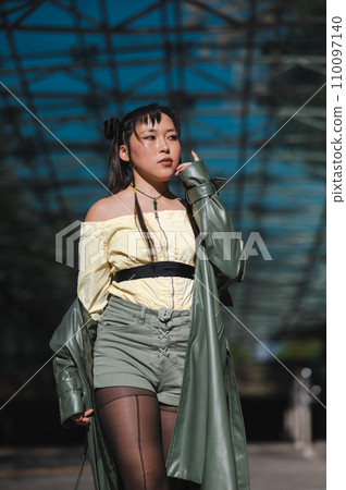 A beautiful Asian woman in shorts and a green leather coat comes out of the subway.  110097140