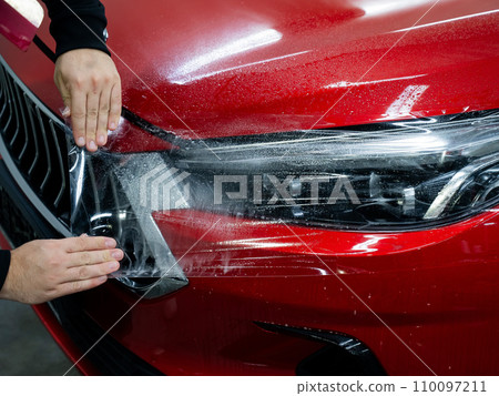 The master applies vinyl film to the headlight of a red car. The master applies vinyl film to the headlight of a red car. 110097211
