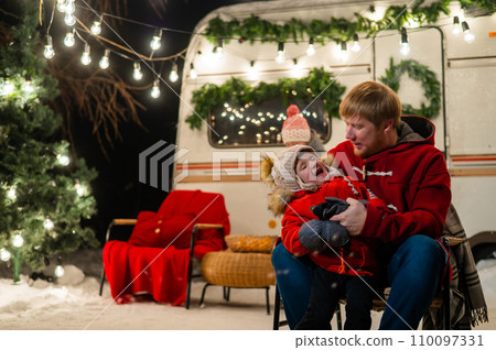 Caucasian red-haired man with a boy in his arms at the mobile home. Father and son celebrate Christmas on a trip. 110097331