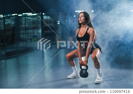 Caucasian woman squats with kettlebell in the gym. Caucasian woman squats with kettlebell in the gym. 110097418