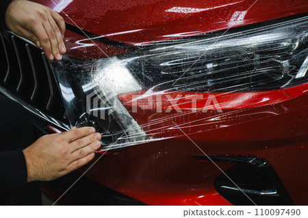 The master applies vinyl film to the headlight of a red car. The master applies vinyl film to the headlight of a red car. 110097490