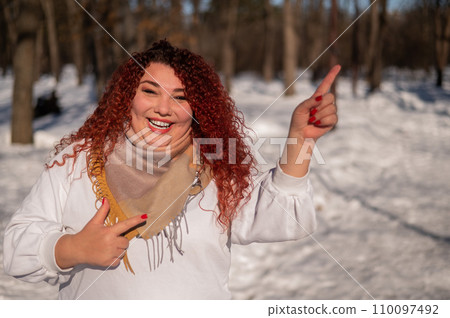 A chubby red-haired woman in a white sweatshirt. Girl fooling around in the park in winter.  110097492