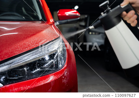 A man washes the headlights of a red car with a spray. A man washes the headlights of a red car with a spray. 110097627