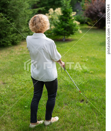 Rear view of an elderly blind woman walking in the park with a tactile cane. Rear view of an elderly blind woman walking in the park with a tactile cane. 110097644